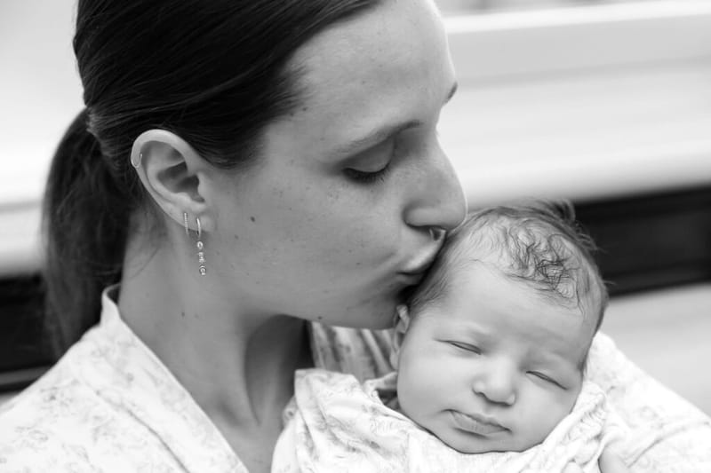 Brooke kissing a sleeping newborn baby on the head in a hospital room, black and white