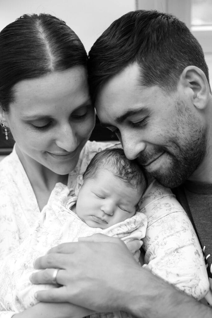 Brooke and her partner leaning in together over their sleeping newborn, black and white hospital photo